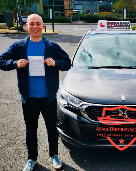 Learner holding a practical driving test pass certificate beside the Alma Driving School grey DS 4