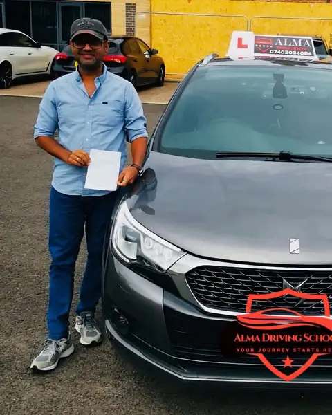 Learner holding a practical driving test pass certificate beside the Alma Driving School grey DS 4