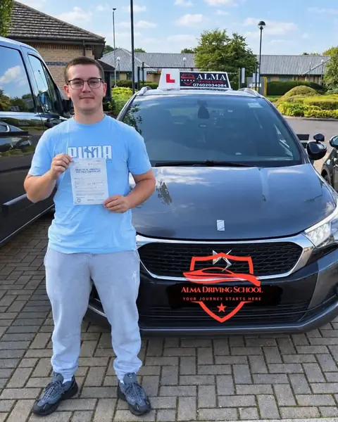 Learner holding a practical driving test pass certificate beside the Alma Driving School grey DS 4
