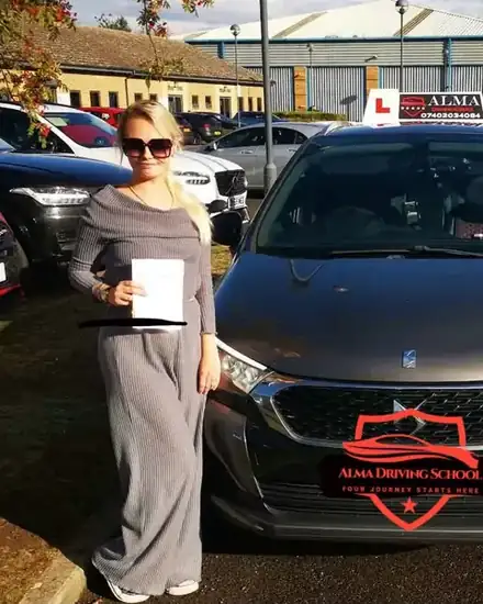 Learner holding a practical driving test pass certificate beside the Alma Driving School grey DS 4